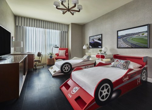 A stylish children's room featuring race car beds, a desk, and large windows with sheer curtains.