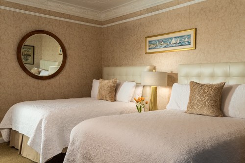 A cozy hotel room with two beds, a round mirror, a lamp, and a vase of tulips on a bedside table.