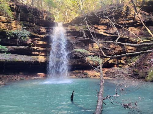 A serene waterfall cascades into a turquoise pool, surrounded by rocky cliffs and lush greenery.