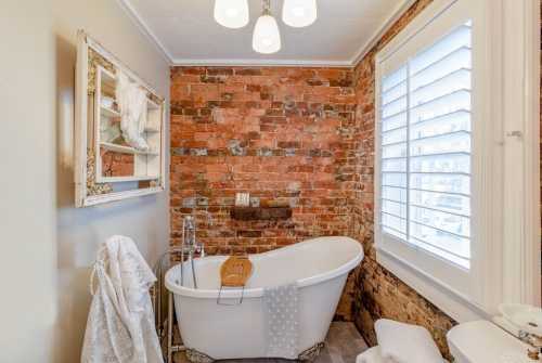 A cozy bathroom featuring a vintage freestanding tub, exposed brick walls, and soft lighting.