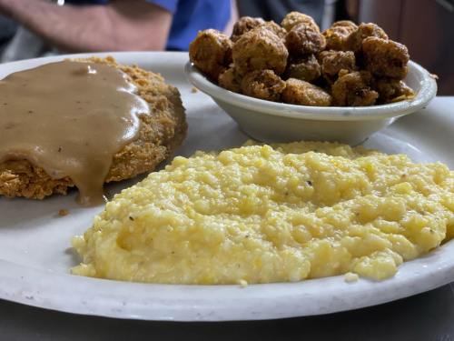 A plate with fried chicken smothered in gravy, creamy grits, and a side of crispy fried okra.