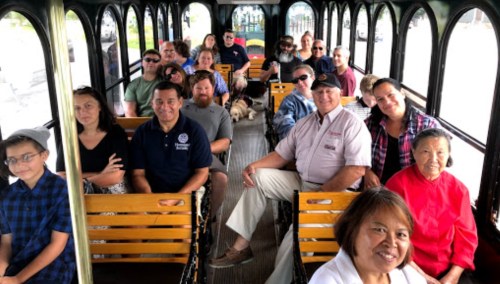 A diverse group of people seated inside a trolley, smiling and enjoying a ride together.