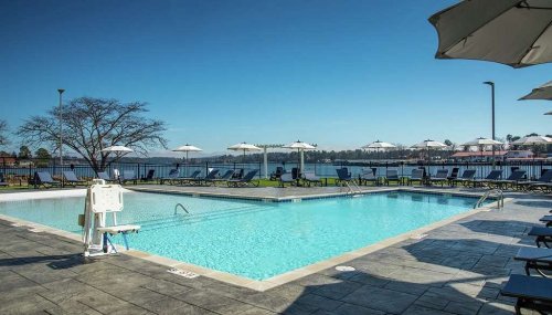 A serene pool area with lounge chairs and umbrellas, overlooking a calm lake under a clear blue sky.
