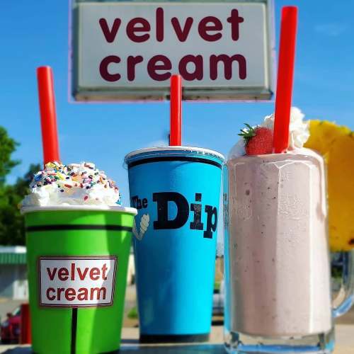 Three colorful ice cream drinks with whipped cream and toppings, displayed under a sign that reads "velvet cream."