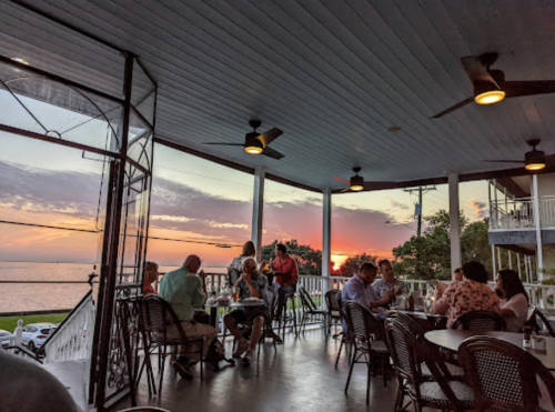 A restaurant patio at sunset, with diners enjoying their meals and a view of the ocean.