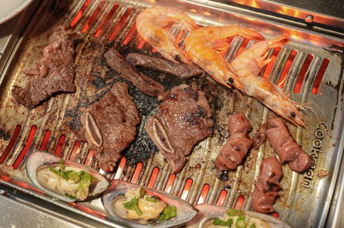 Grilled meats and shrimp on a barbecue grill, with a variety of seafood and beef sizzling over flames.