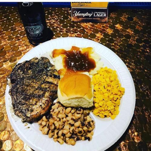 A plate with seasoned grilled chicken, mashed potatoes with gravy, corn, black-eyed peas, a roll, and a soda.