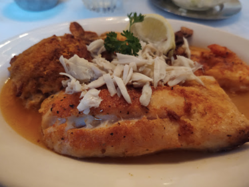 A plate of golden-brown fish topped with shredded crab meat, garnished with lemon and parsley.