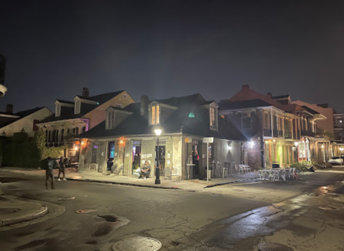 A dimly lit street corner at night, featuring historic buildings and a few people walking by.