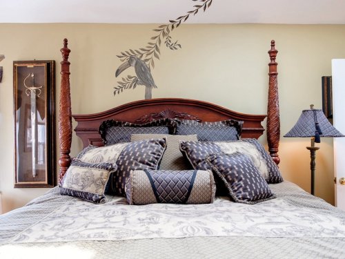 A beautifully decorated bed with an ornate headboard, plush pillows, and a wall mural of a bird and leaves.
