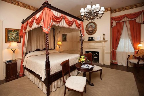 A cozy bedroom featuring a four-poster bed, elegant decor, a chandelier, and a seating area with a small table.