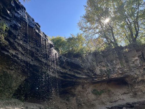A serene landscape featuring a waterfall cascading over rocky cliffs, surrounded by lush greenery and a clear blue sky.
