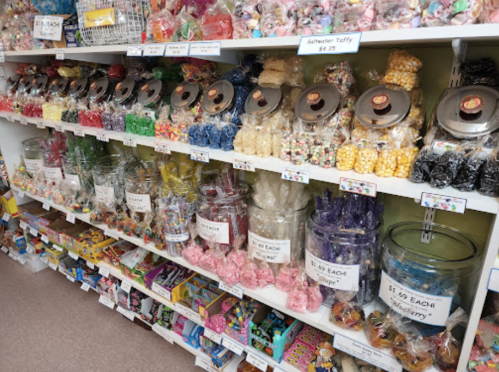A colorful display of various candies in jars and bags on shelves, with price tags visible.