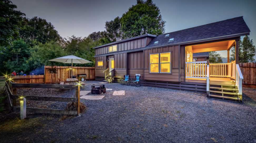 A modern home with a spacious backyard, featuring a patio, fire pit, and outdoor seating, illuminated at dusk.