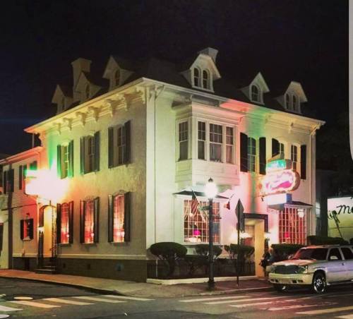 A historic building at night, featuring colorful lights and large windows, with a car parked outside.