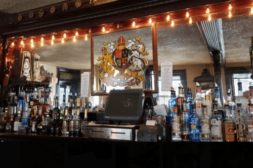 A bar counter filled with various bottles of liquor, featuring a decorative mirror and warm string lights.