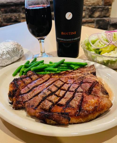 A grilled steak on a plate with green beans, a side salad, a glass of red wine, and a bottle of Fantini wine.