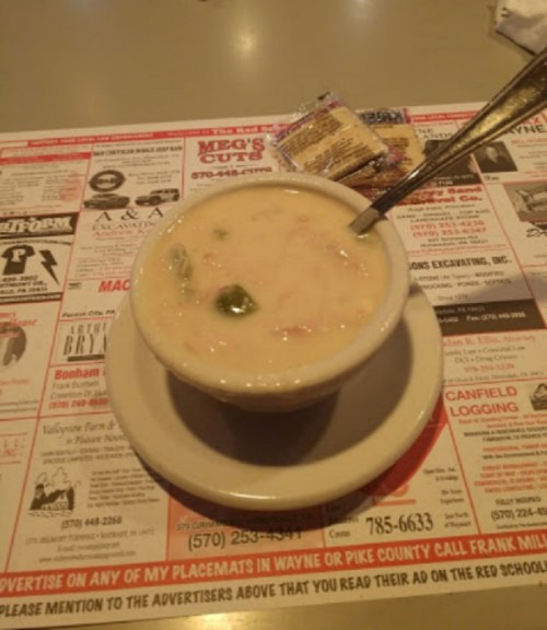 A bowl of creamy soup with vegetables, placed on a colorful restaurant menu with a spoon beside it.