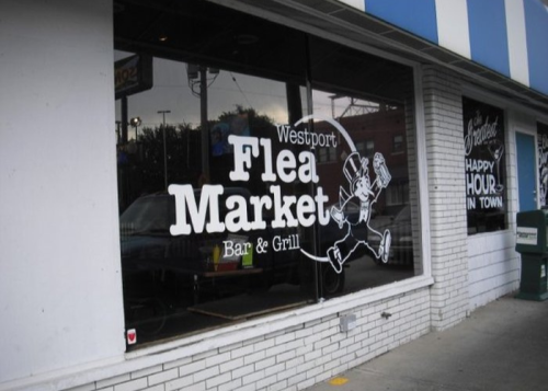 Exterior of Westport Flea Market Bar & Grill, featuring a large window sign with a cartoon character and striped awning.
