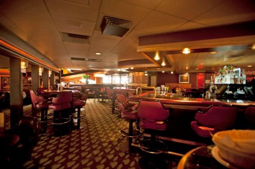 A dimly lit bar interior featuring purple stools, a long counter, and a patterned carpet.