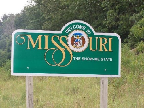 Welcome sign for Missouri, featuring the text "The Show-Me State" and a state seal, set against a green background.