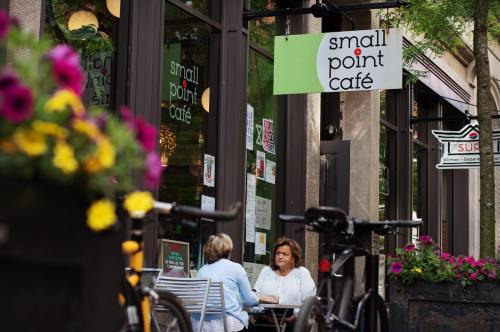 Two women sit at a table outside Small Point Café, surrounded by flowers and a bicycle parked nearby.