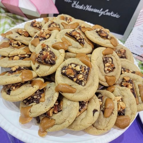 A plate of freshly baked cookies topped with chocolate, caramel, and chopped nuts, arranged neatly.