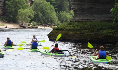 A group of people kayaking on a river surrounded by lush greenery and rocky cliffs.