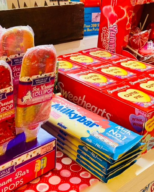 Colorful display of candy, including ice cream lollipops, Sweethearts, and Milky Bars on a table.