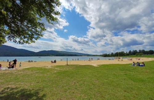 A sandy beach with people enjoying the sun, surrounded by green hills and a partly cloudy sky.
