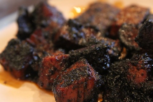 Close-up of dark, charred pieces of meat glistening with sauce on a plate.