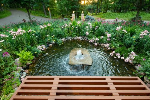 A serene garden pond with a fountain, surrounded by colorful flowers and lush greenery, under a warm sunset.