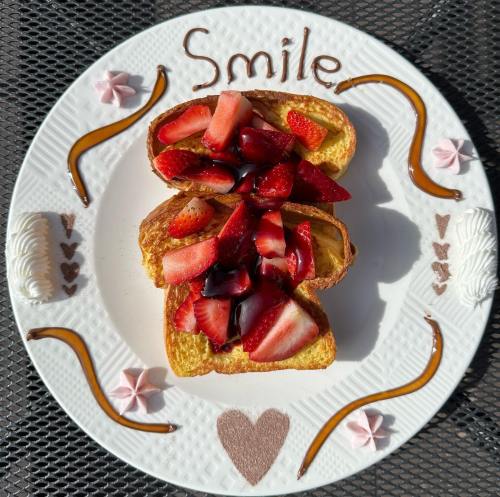A plate with two slices of French toast topped with strawberries and chocolate, decorated with "Smile" and heart shapes.