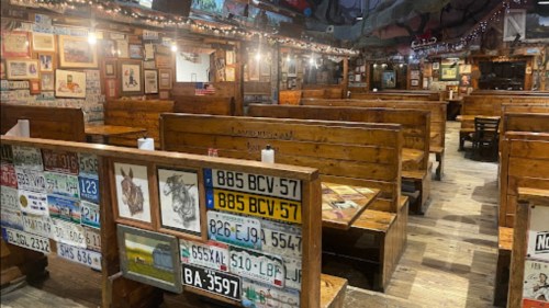 Interior of a rustic restaurant with wooden booths, vintage license plates, and framed artwork on the walls.