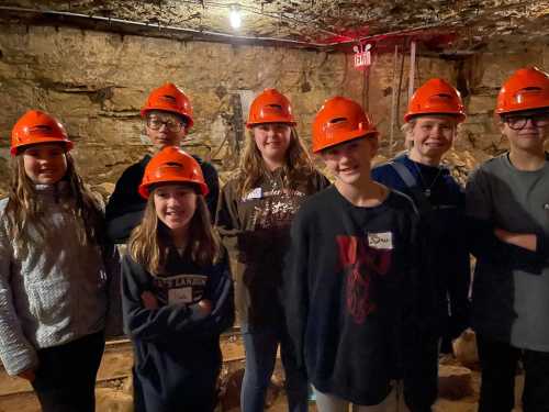 A group of children wearing orange helmets smiles in a dimly lit cave.