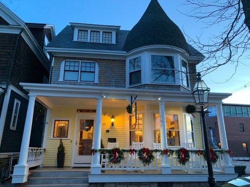 A charming Victorian-style house decorated with holiday wreaths, featuring a turret and a welcoming porch at dusk.