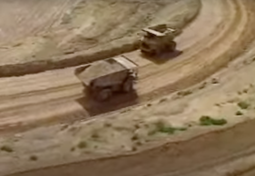 Two large mining trucks navigate a winding dirt road in a quarry.