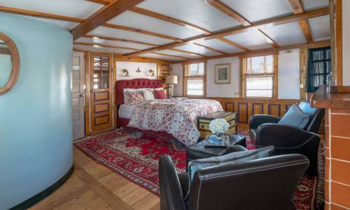 Cozy bedroom with a red upholstered bed, floral bedding, wooden accents, and a seating area with black chairs.