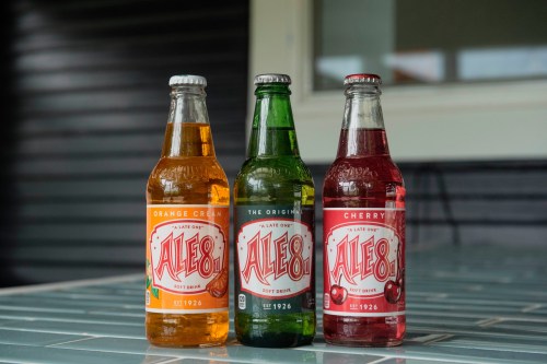 Three bottles of Ale-8 soft drinks: orange cream, original green, and cherry, displayed on a tiled surface.