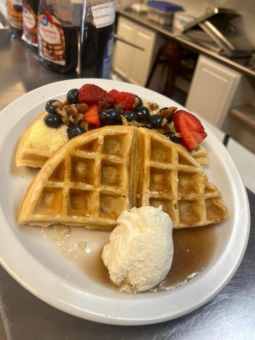 A plate of waffles topped with fresh berries, nuts, and a scoop of ice cream, drizzled with syrup.