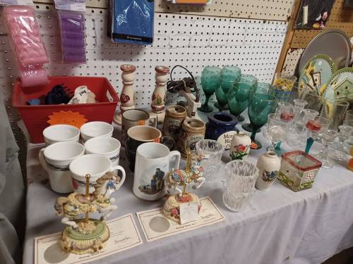 A variety of vintage glassware, ceramics, and decorative items displayed on a table in a thrift store.