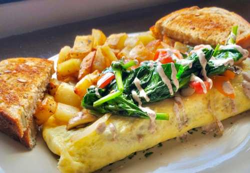 A plate featuring a spinach and vegetable omelet, seasoned potatoes, and two slices of toasted bread.