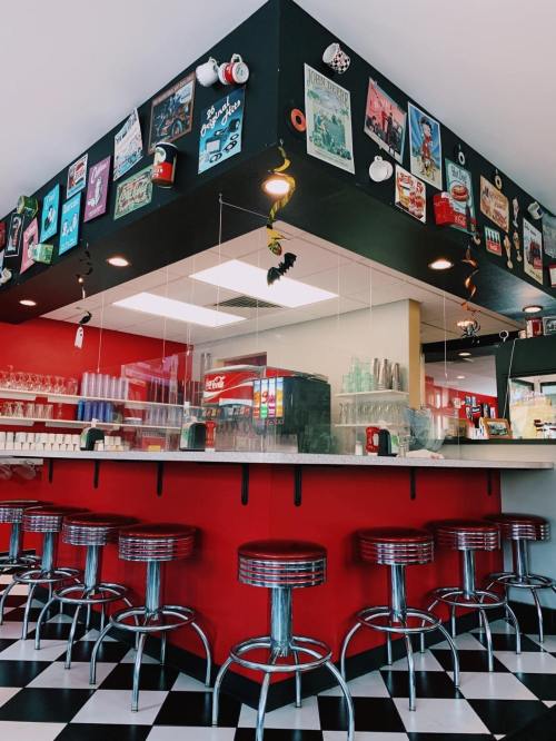 A retro diner interior with a red and black color scheme, featuring bar stools and vintage posters on the walls.