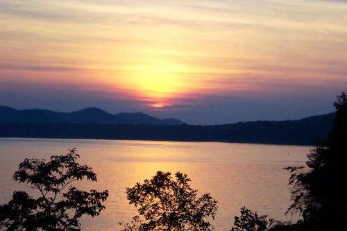 A serene sunset over a lake, with mountains in the background and soft colors reflecting on the water.