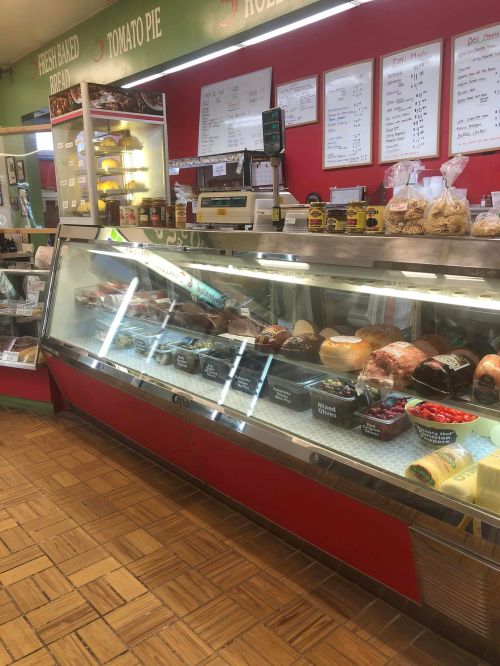 Deli counter displaying various meats, cheeses, and condiments in a bright, inviting shop interior.