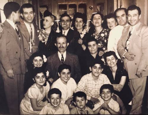 A large group of people, including men, women, and children, posing together in a vintage setting.