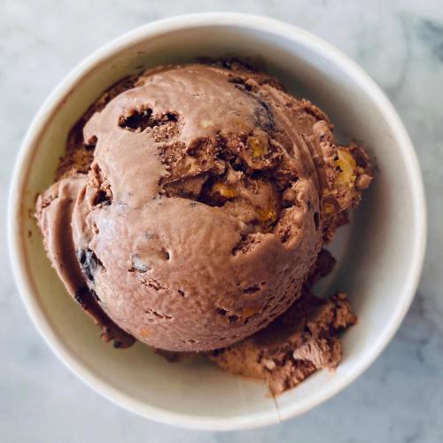 A scoop of chocolate ice cream with chunks, served in a white paper cup on a marble surface.