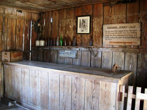 Interior of an old saloon with a wooden bar, rustic walls, and a sign about the Original Jersey Lilly.