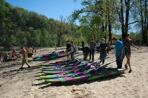 A group of people on a sandy shore preparing colorful kayaks for a day of paddling on a sunny day.
