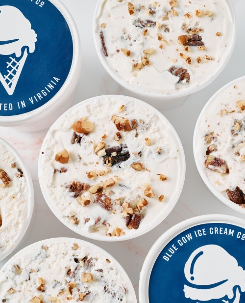 Several tubs of ice cream with nuts on top, featuring a blue lid that says "Blue Cow Ice Cream Co." and "Made in Virginia."